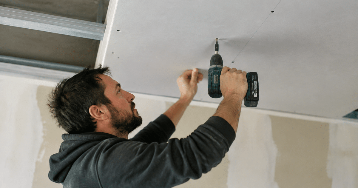 Ouvrier fixant panneau placo blanc au plafond avec vis