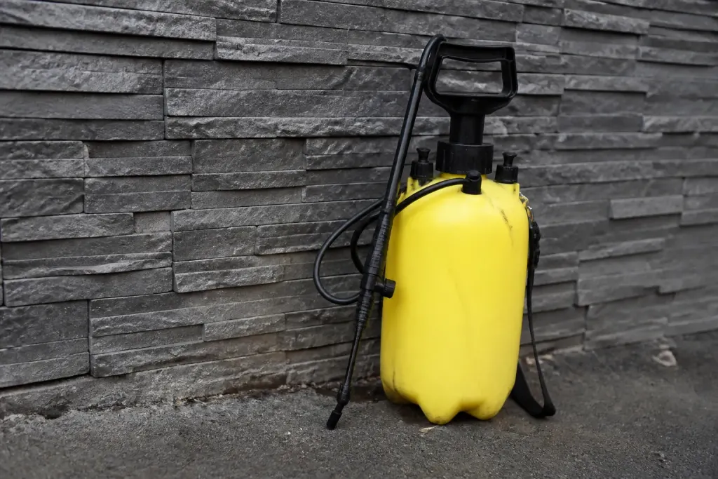 Pulverisateur jaune a pression pose contre un parement gris